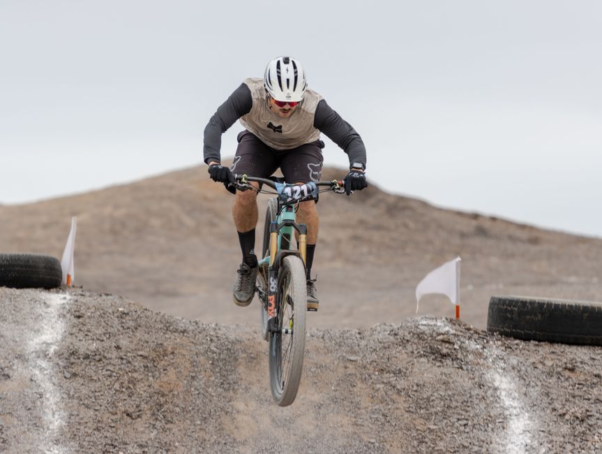 Mountain biker jumping over dirt mound on a challenging desert trail in daylight.