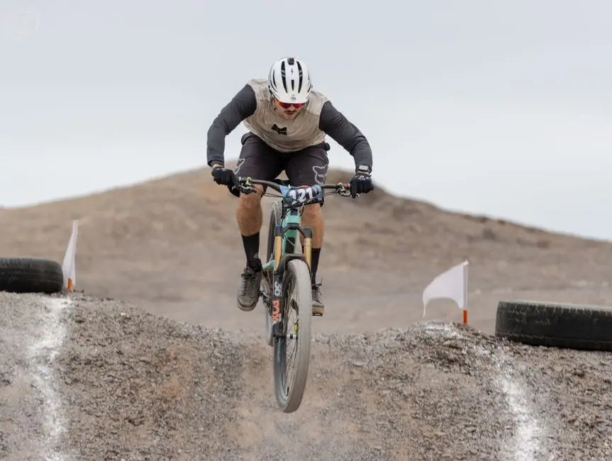 Mountain biker jumping over dirt mound on a challenging desert trail in daylight.