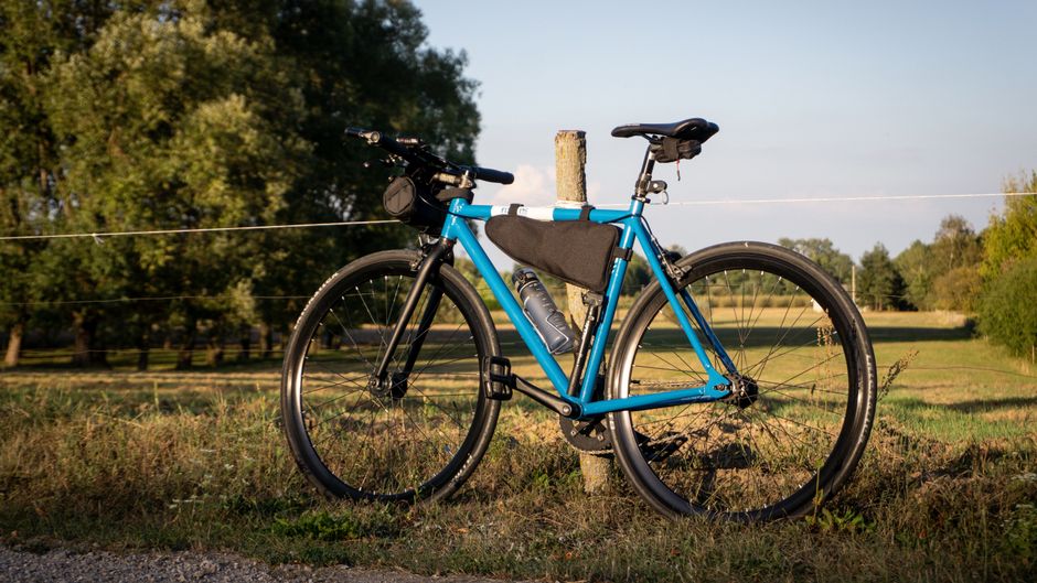 A blue road bike parked by a wooden post in a sunny field in Warsaw, Poland.