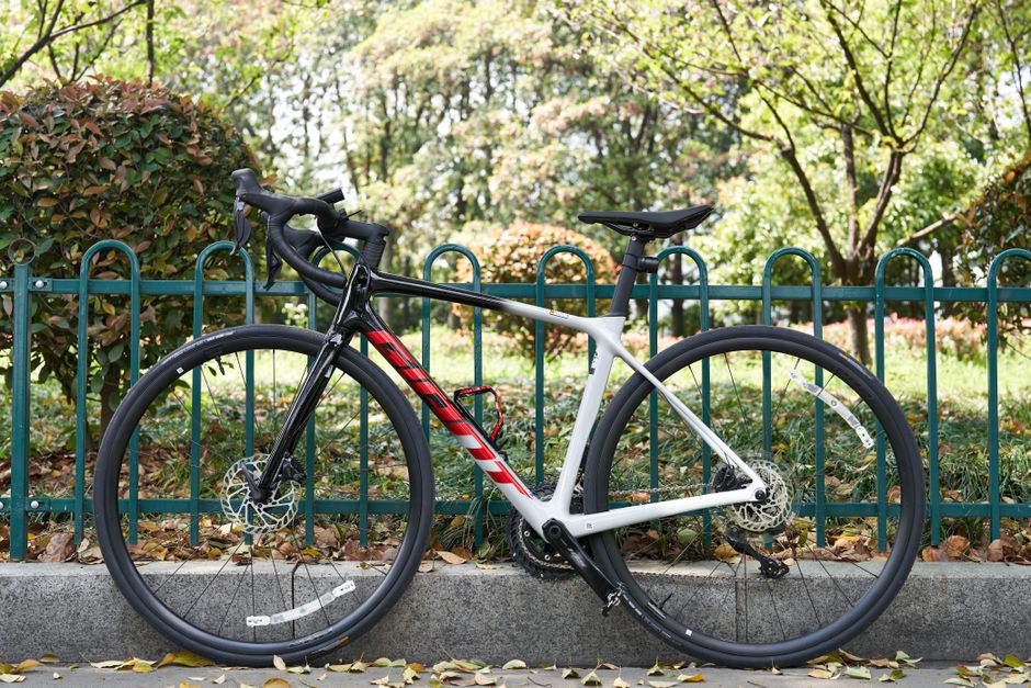 A sleek modern road bike is parked along a park fence amidst autumn leaves.