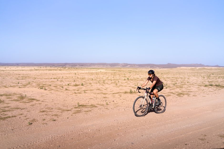 Cyclist crosses expansive desert terrain under clear blue skies, embodying adventure.