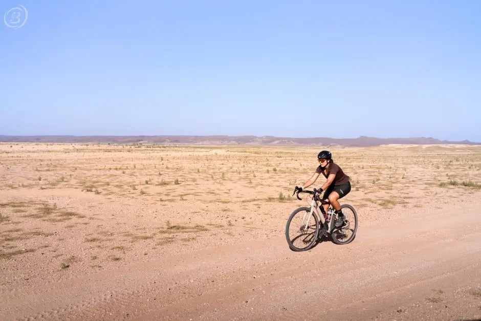 Cyclist crosses expansive desert terrain under clear blue skies, embodying adventure.