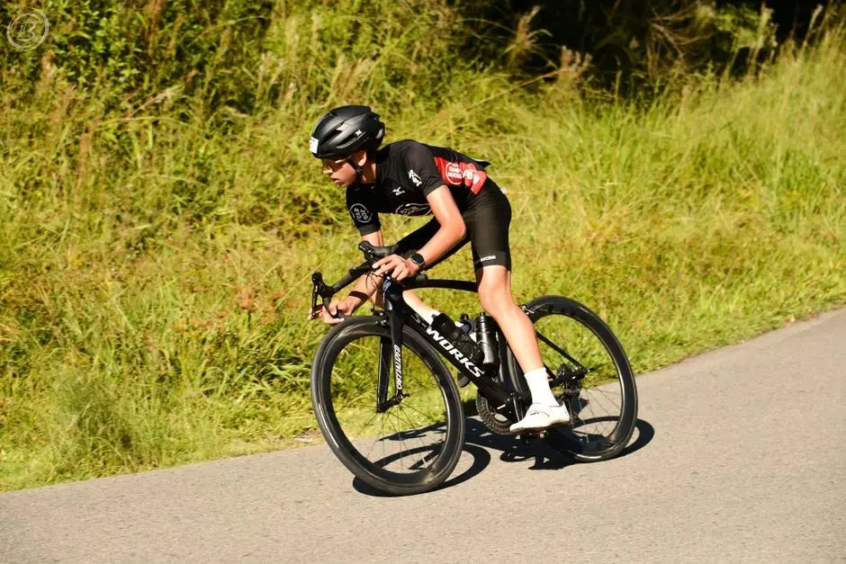 Competitive cyclist riding fast on a road surrounded by greenery under a clear blue sky.